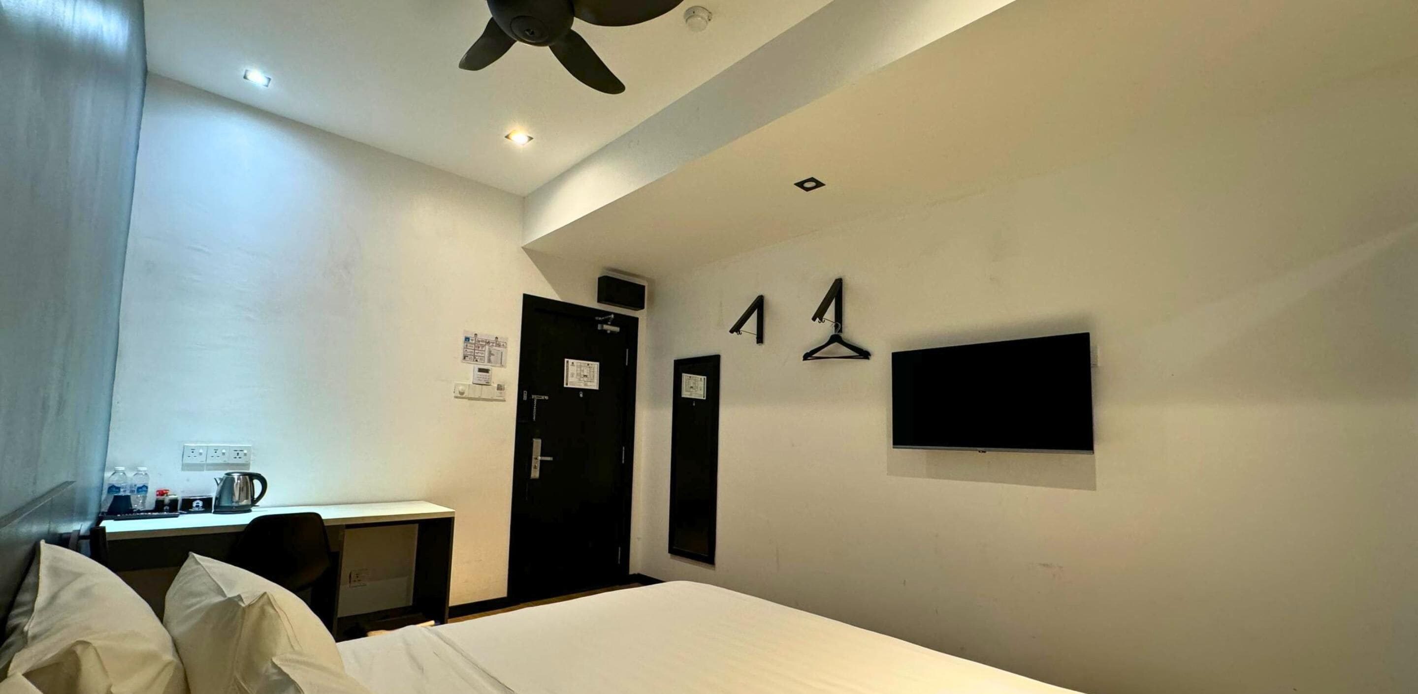 A hotel room with a bed, desk, and a TV mounted on the wall.