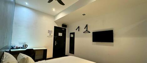 A hotel room with a bed, desk, and a TV mounted on the wall.