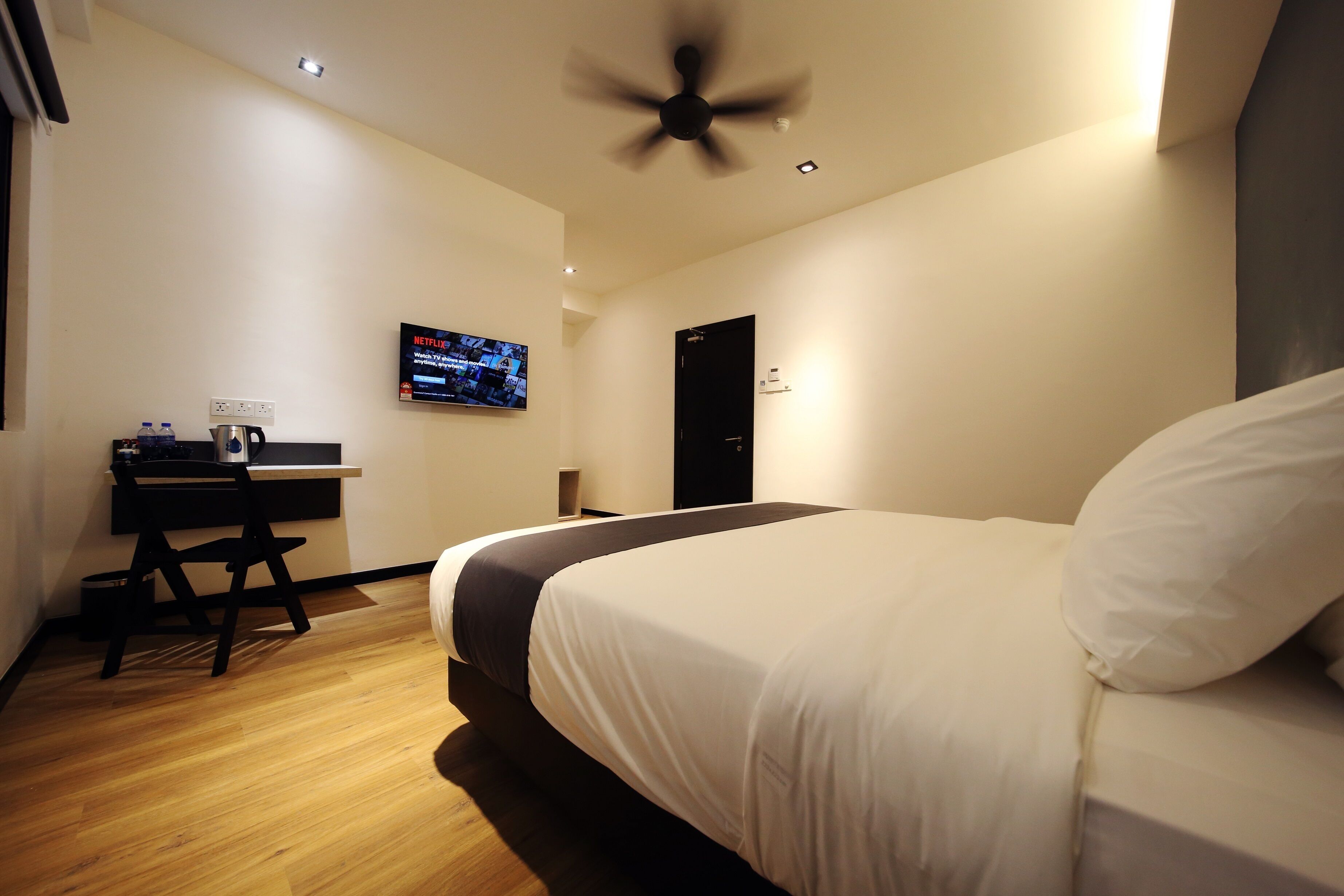 Une chambre d’hôtel équipée d’un lit, d’un bureau avec un ordinateur, d’une télévision et d’un ventilateur de plafond.