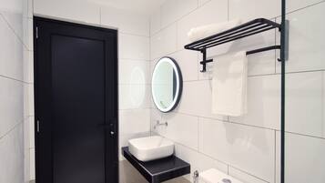 A modern bathroom with a black door, white tiles, a round mirror, a white sink, and a toilet.