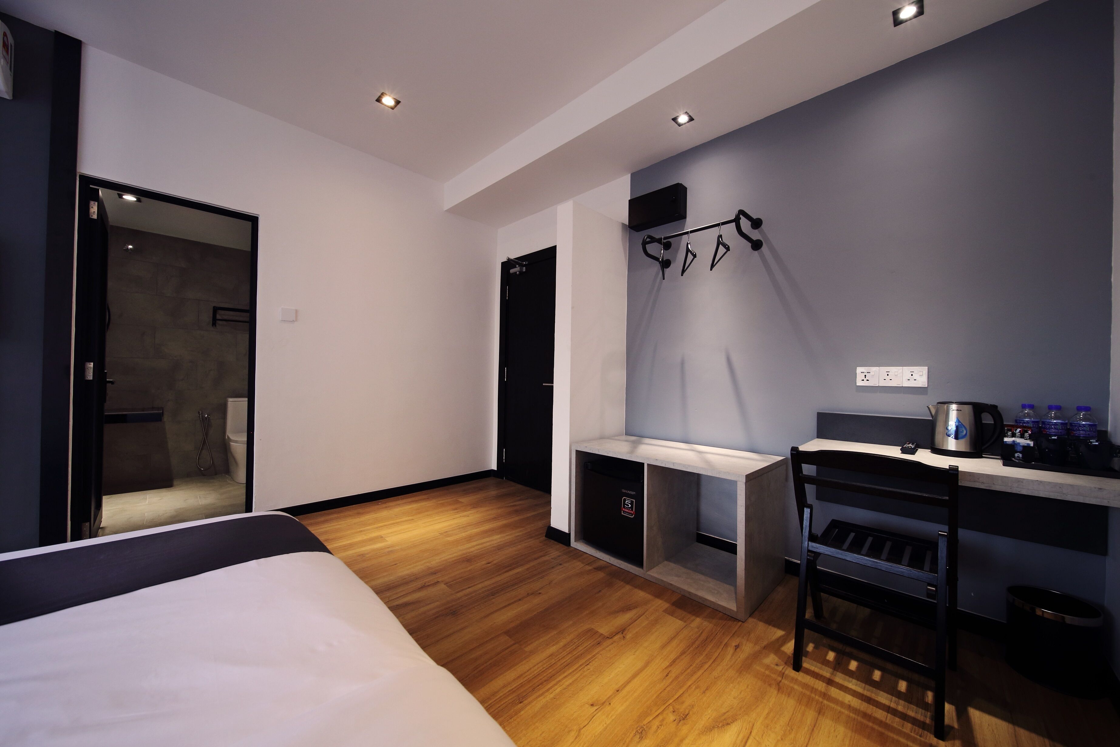 A modern hotel room with a bed, a desk with a kettle, and a shower area.