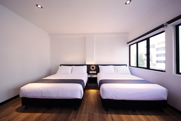 Habitación de hotel con dos camas individuales, una mesita de noche pequeña y un gran ventanal con vistas al exterior.