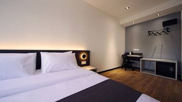 A modern hotel room with a large bed, a desk, and a small seating area.
