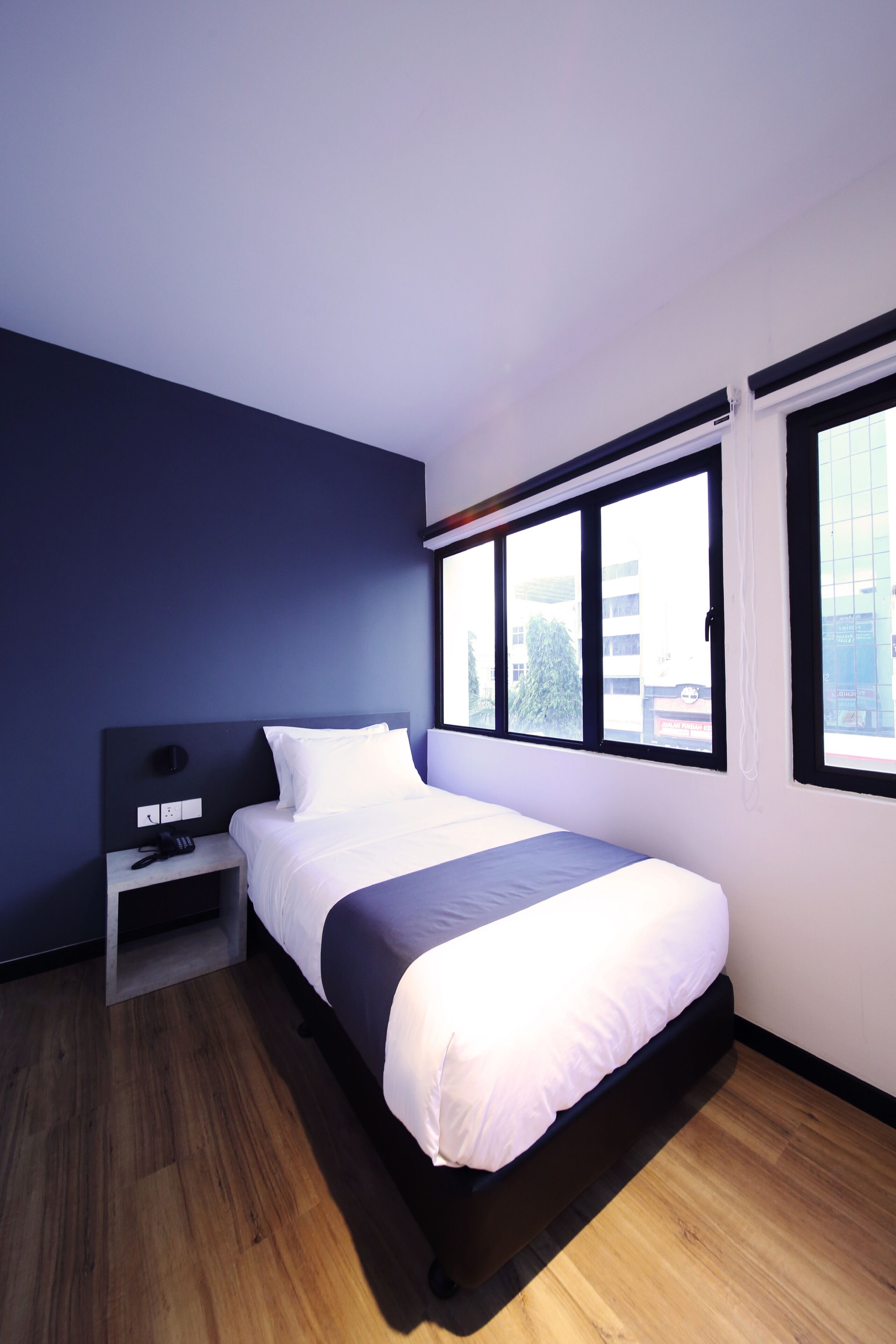 A modern hotel room with a large bed, a bedside table, and a window with a view of the city.