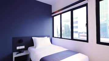 A modern hotel room with a large bed, a bedside table, and a window with a view of the city.