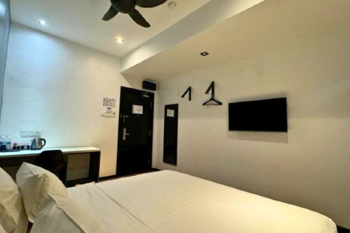 A hotel room with a bed, a desk, a chair, and a TV mounted on the wall.