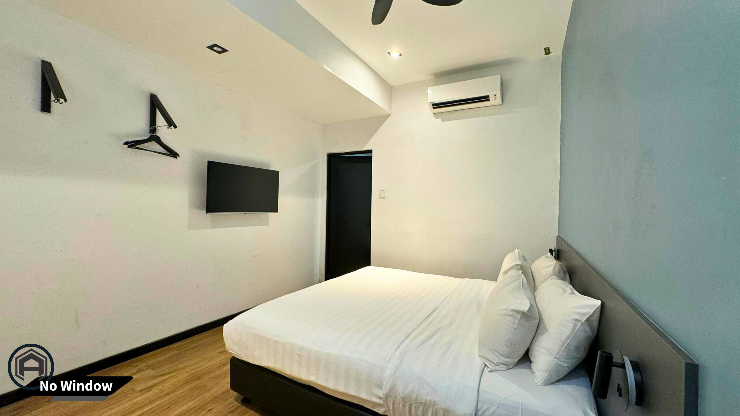A bedroom with a bed, pillows, a flat-screen TV, an air conditioner, and a door.