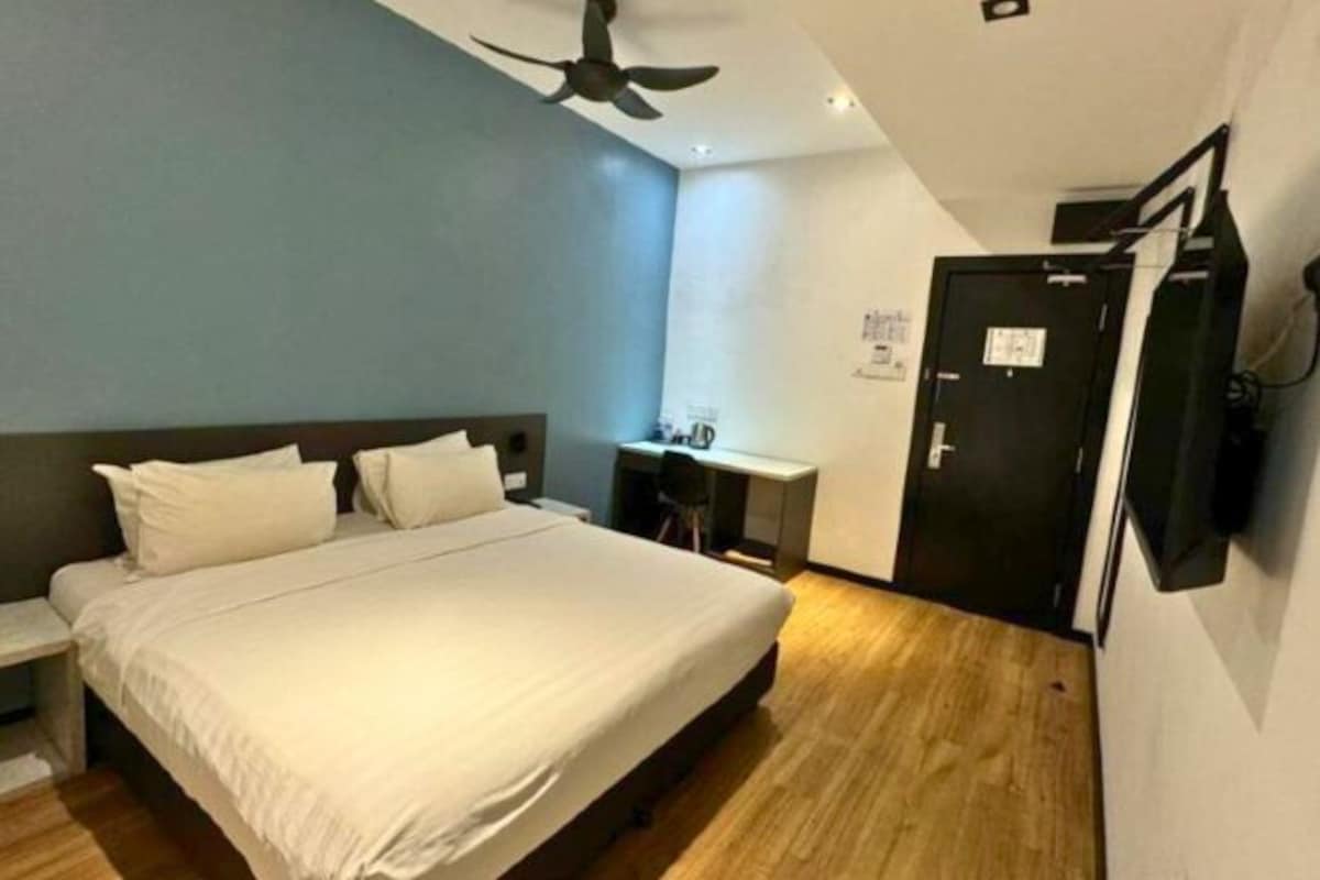 A bedroom with a bed, a desk, a chair, a ceiling fan, and a door.
