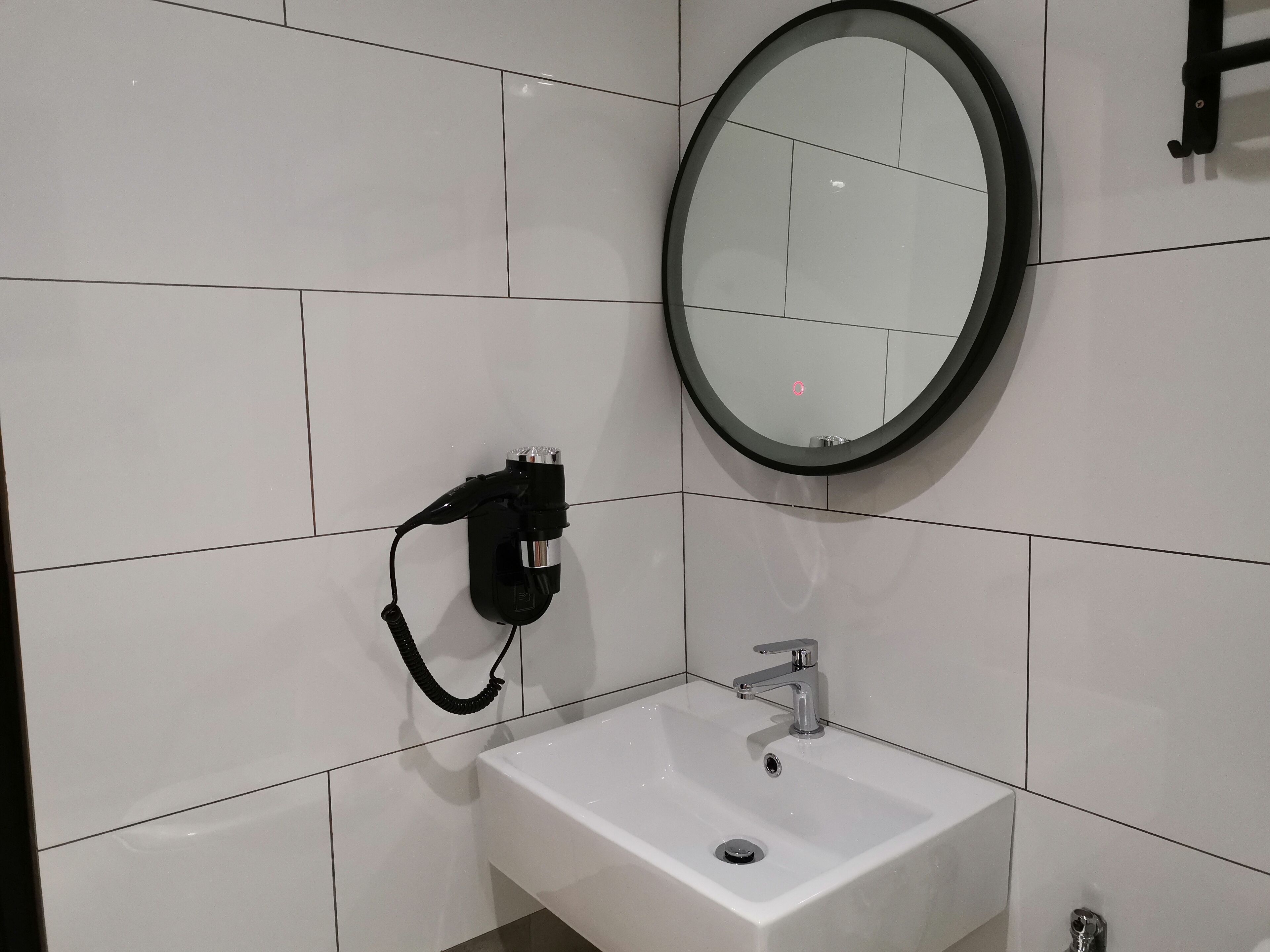 Un baño con un lavamanos blanco, un espejo y un enchufe eléctrico negro.
