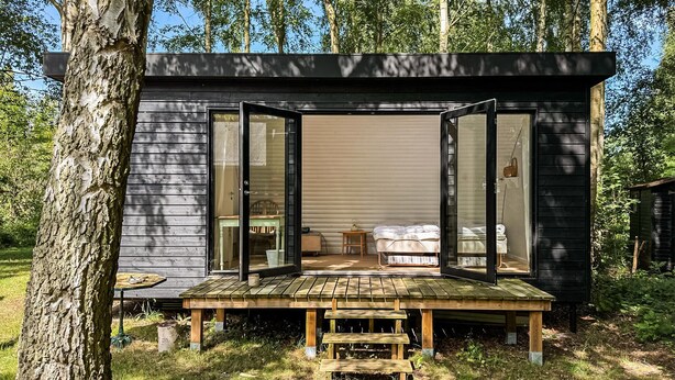 Une petite cabane dont la porte est ouverte, laissant apercevoir un lit et une table à l’intérieur.