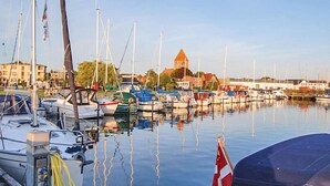 Un port de plaisance où sont amarrés de nombreux bateaux, un bâtiment imposant surmonté d’une tour et un ciel dégagé.