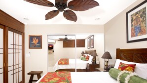 Ein Hotelzimmer mit Bett, Deckenventilator, Holz-Kopfteil, Nachttisch und kleinem Tisch.