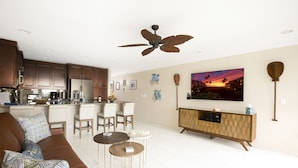 Ein modernes Wohnzimmer mit einem braunen Sofa, zwei runden Couchtischen, einem Wandfernseher und einem Holzschrank.