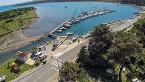 Vista aérea de uma marina com barcos atracados, uma estrada que leva à marina e vegetação ao redor.