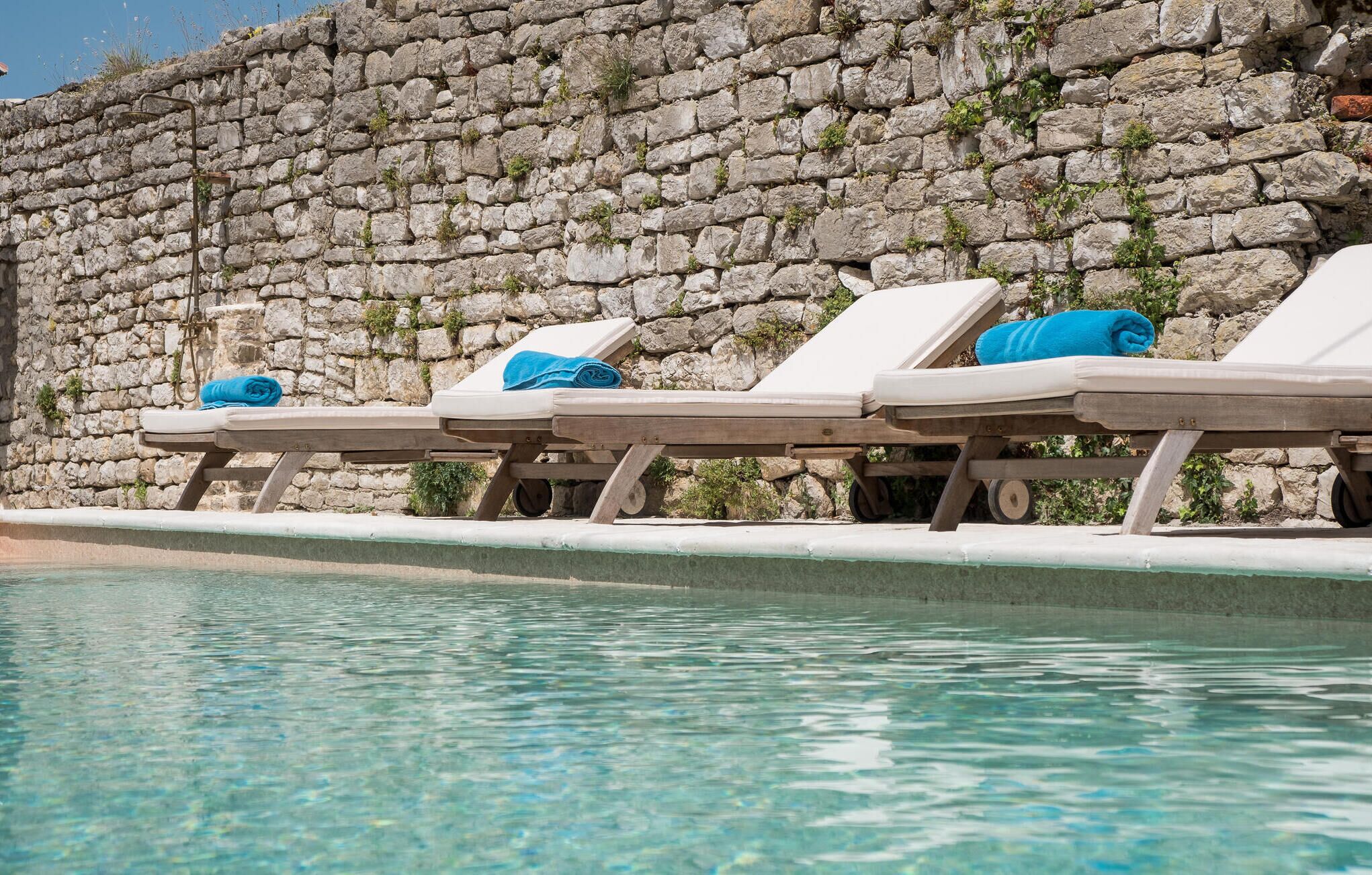 Un espace aménagé au bord de la piscine, avec des chaises longues et un mur en pierre.