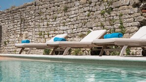 Área à beira da piscina com espreguiçadeiras e uma parede de pedra.