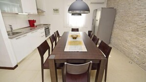 A modern kitchen with white cabinets, a dining table with chairs, a pendant light, and a brick wall.