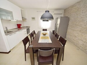 A modern kitchen with white cabinets, a dining table with chairs, a pendant light, and a brick wall.