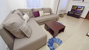 A living room with a beige sectional sofa, a dark wooden coffee table, and a TV on a stand.