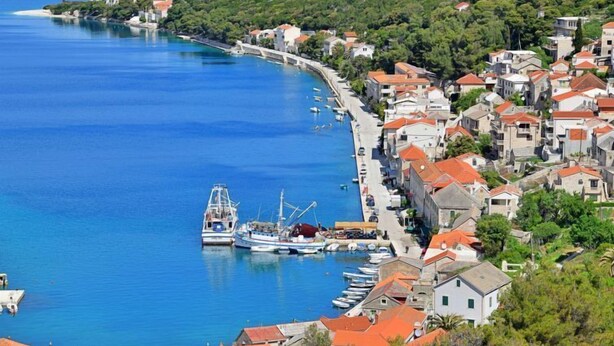 A coastal town with a marina, houses with red roofs, and a clear blue sea.
