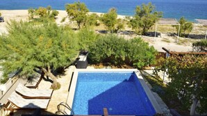 A pool area with lounge chairs, surrounded by trees and a view of the sea and mountains.