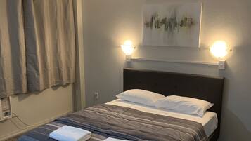 A neatly made bed with a headboard, two bedside lamps, a ceiling fan, and a painting on the wall.