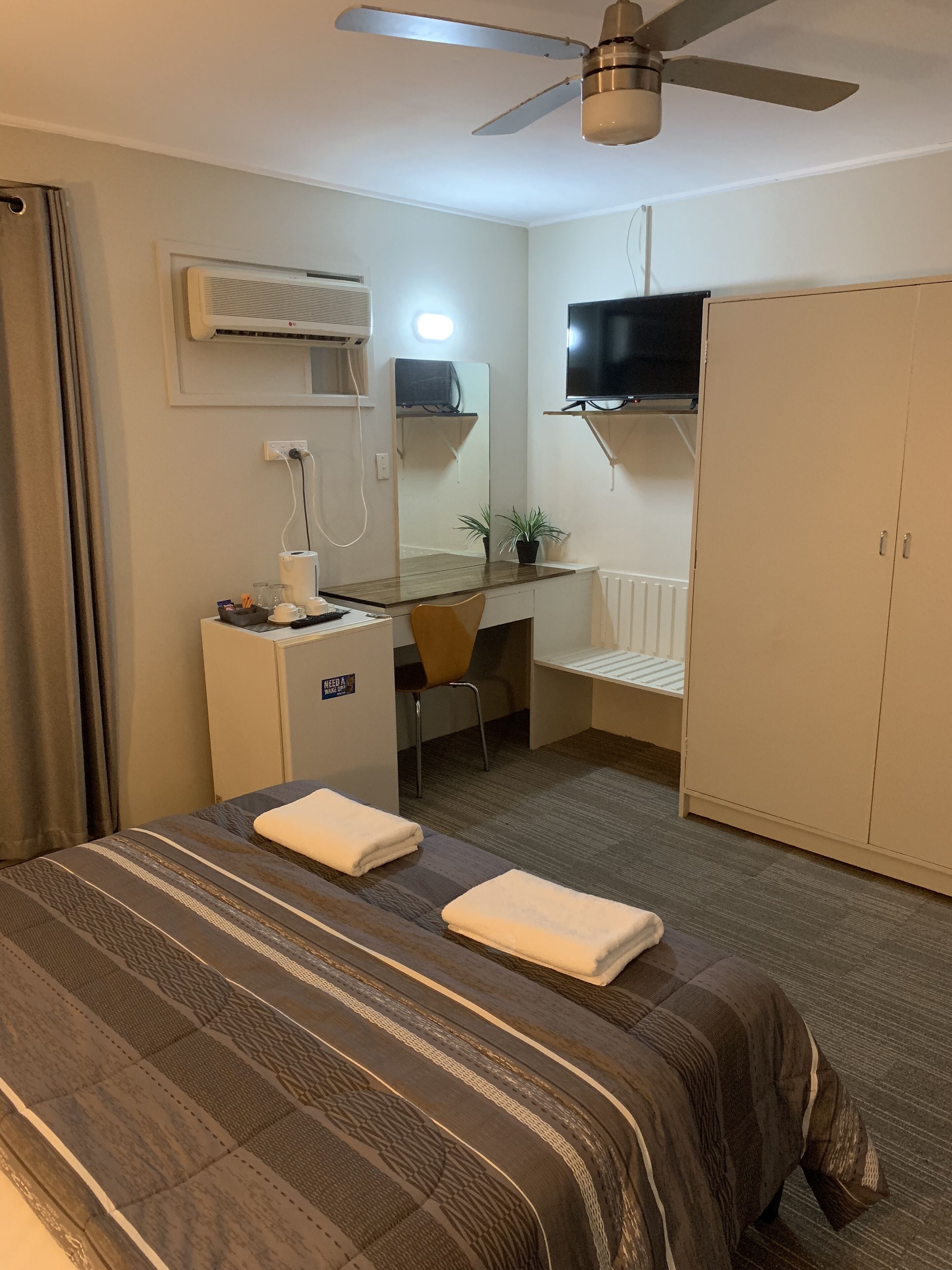 Une chambre d’hôtel équipée d’un lit, d’un bureau, d’une chaise, d’une télévision, d’une armoire et d’un ventilateur de plafond.