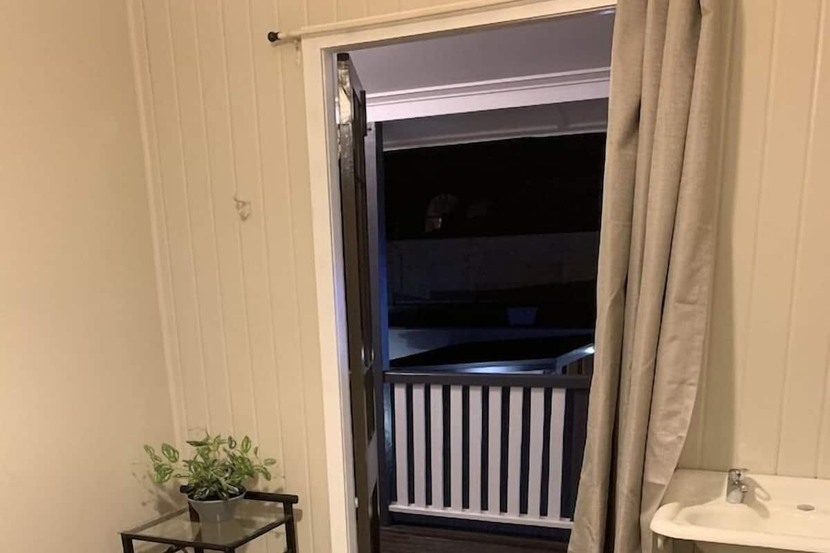 A bedroom with a bed, a small table with a plant, a bathroom with a sink, and a balcony with a railing.
