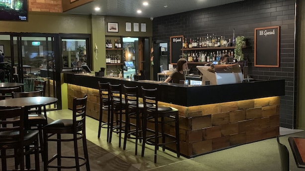 A bar area with wooden bar counter, stools, and a seating area with tables and chairs. - Biloela Hotel (Biloela)
