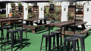 Outdoor tables and benches with umbrellas, surrounded by potted plants and a white wall. - Biloela Hotel (Biloela)