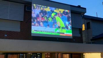 A sports event on a large screen at a venue with a brick facade and a flat roof.