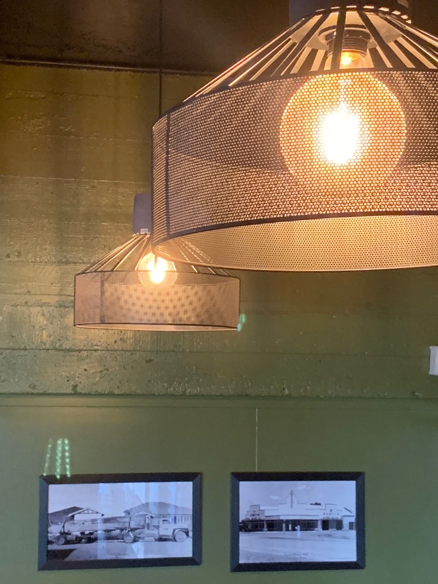 A hanging industrial-style light fixture with a perforated metal design and two bulbs. Below, there are two framed black and white photographs on a green wall.