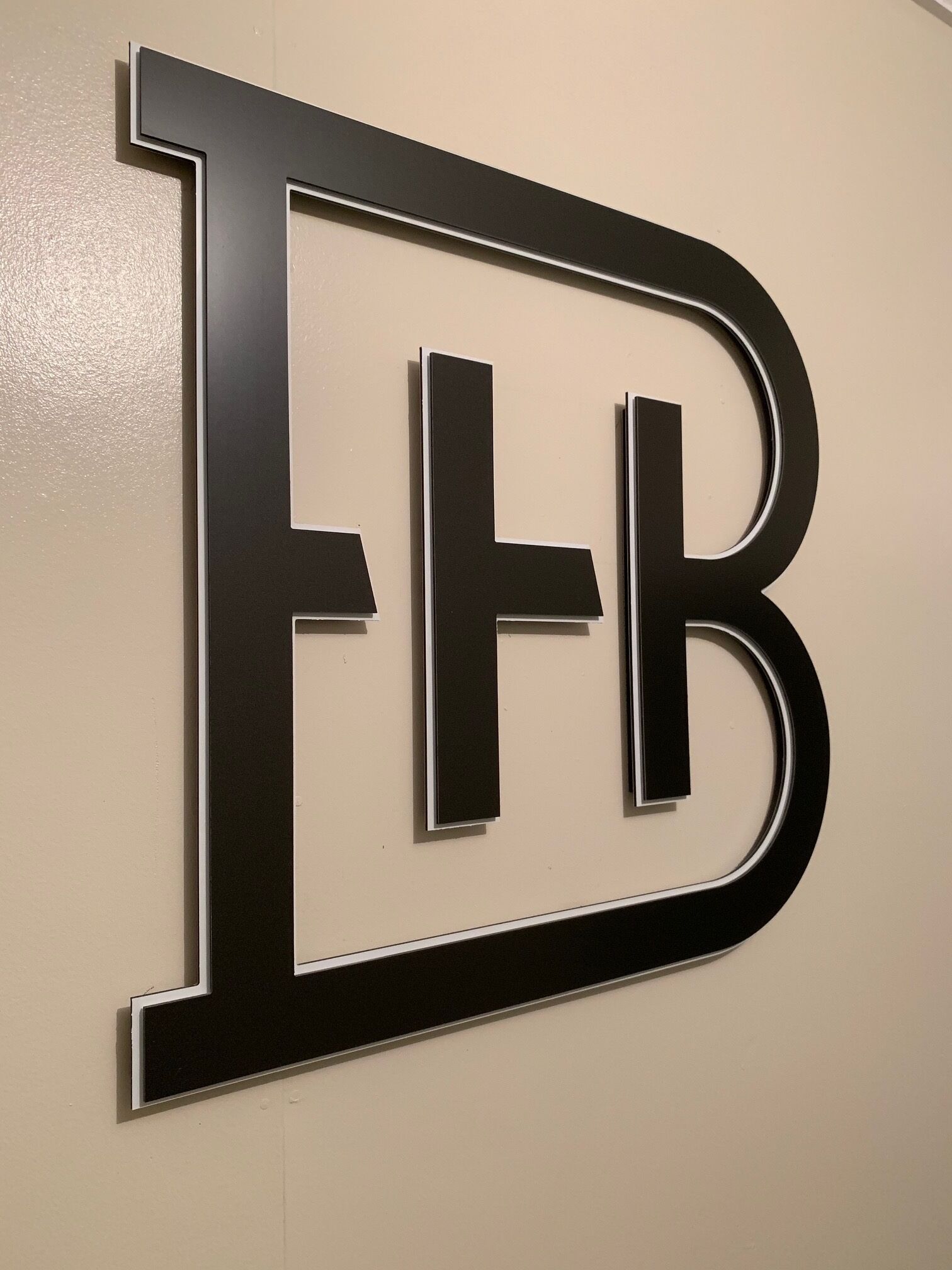 A large, bold, black letter 'B' with a white outline, mounted on a wall.