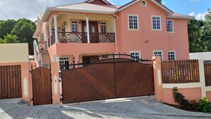 A two-story house with a large wooden gate, a balcony, and a well-maintained garden. - Airconditioned suite (Castries)