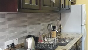 A kitchen with dark cabinets, a granite countertop, a stove, a sink, and a refrigerator. - Airconditioned suite (Castries)