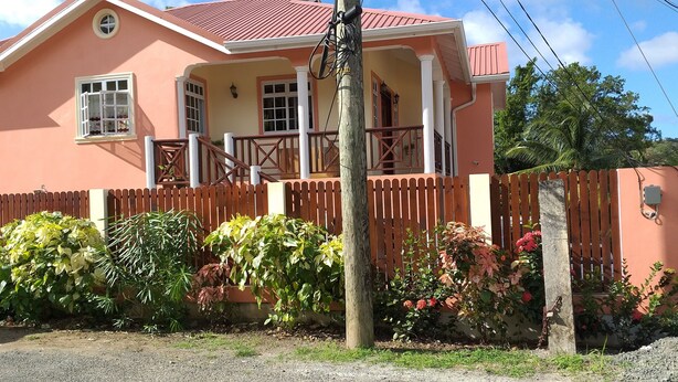 A two-story house with a porch, a wooden fence, and various plants. - Airconditioned suite (Castries)