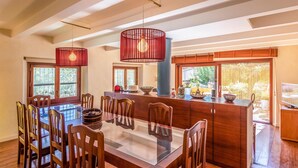 Un comedor amplio con una mesa de vidrio rodeada de sillas de madera, una barra de madera y lámparas colgantes.