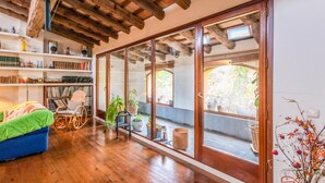 Una habitación amplia con suelo de madera, un gran ventanal corredera que da a un espacio exterior, y un sofá azul.