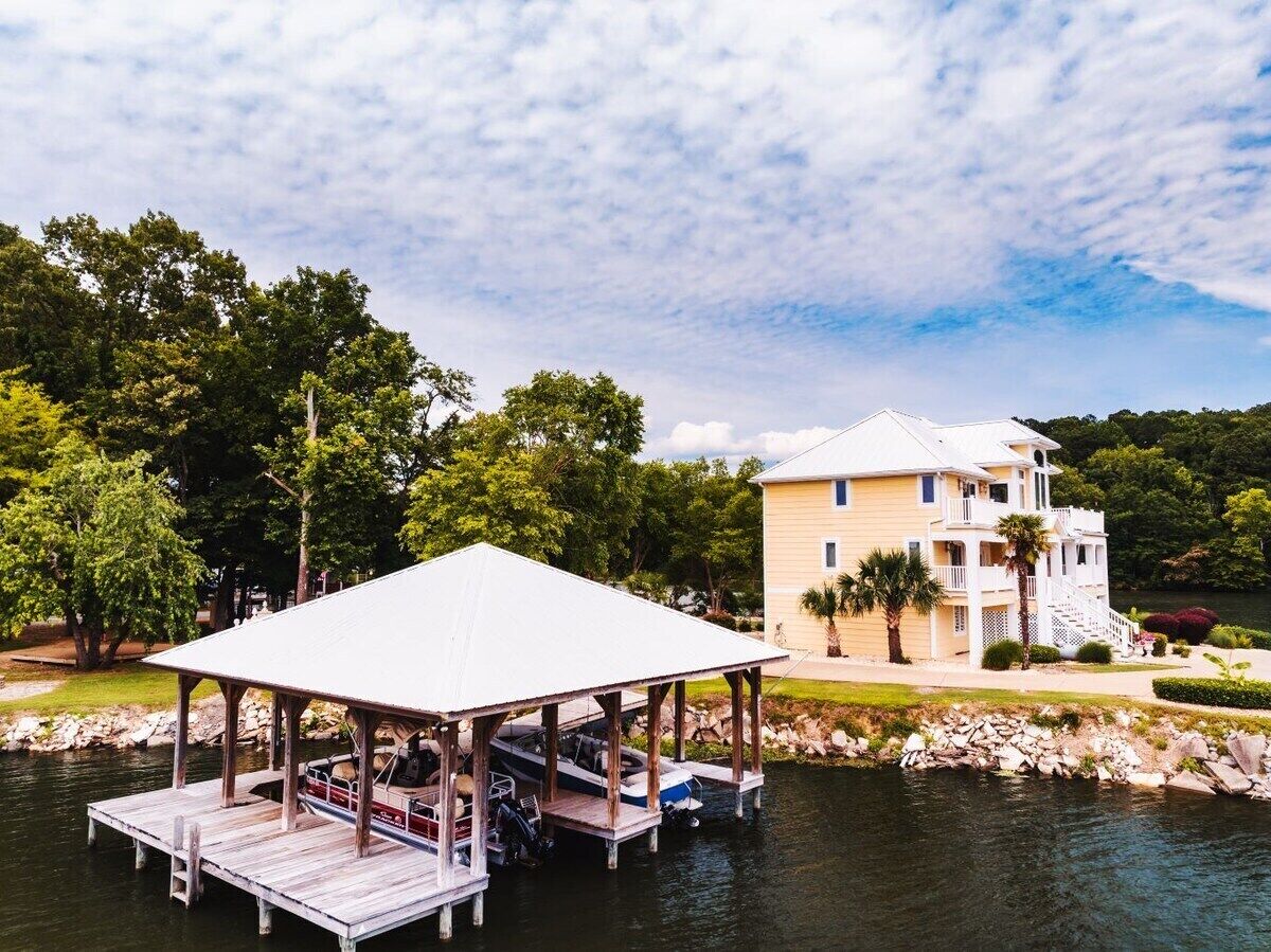 A waterfront property with a dock, a covered boat house, and a large house with multiple levels and balconies.