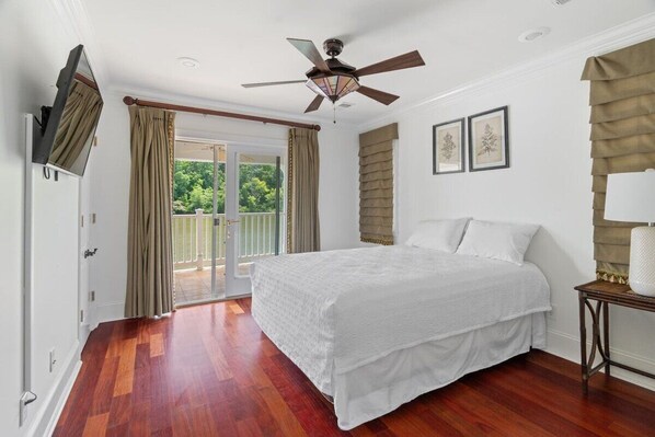A bedroom with a large bed, a ceiling fan, a sliding glass door to a balcony, and a framed picture on the wall.