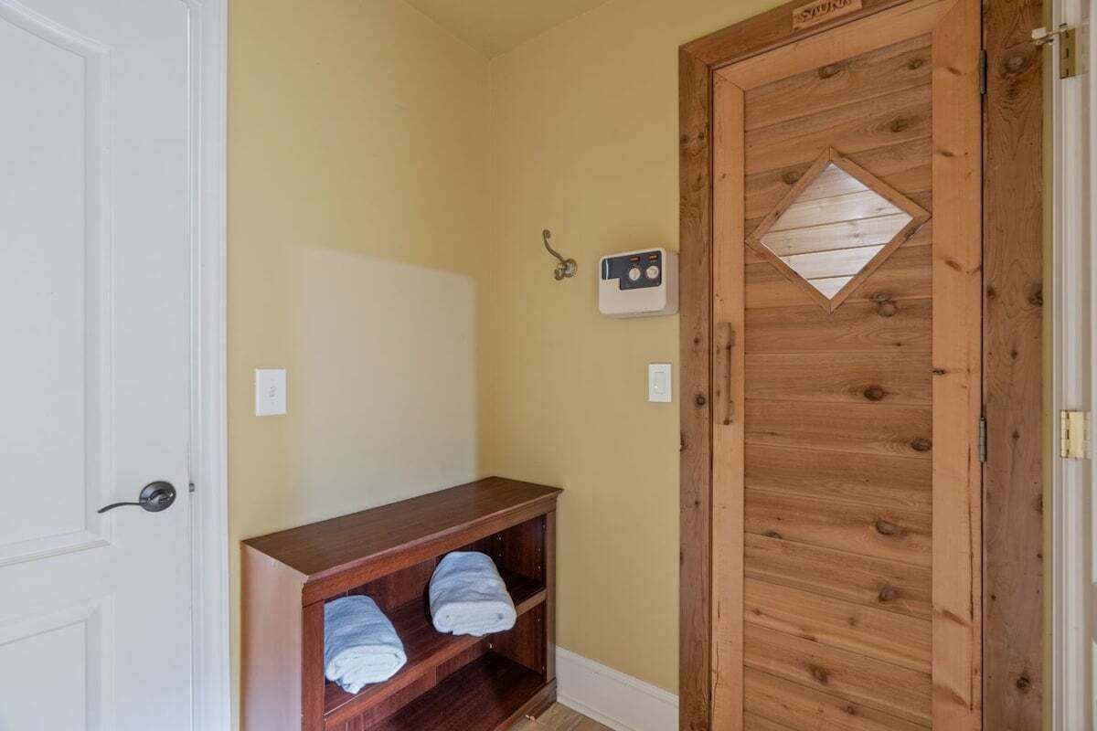 Eine Holztür mit einem rautenförmigen Fenster, ein an der Wand befestigtes Thermostat und ein Holzregal mit Handtüchern.