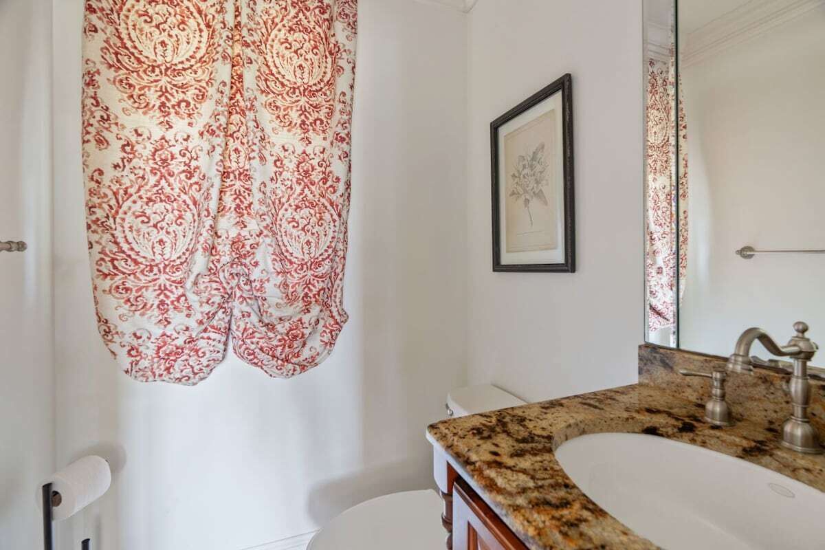 A bathroom with a white toilet, a sink with a granite countertop, and a shower curtain with a paisley pattern.