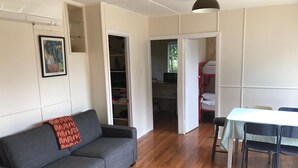 Une pièce avec un canapé gris, une table à manger avec des chaises, une armoire et une porte donnant sur une autre pièce.