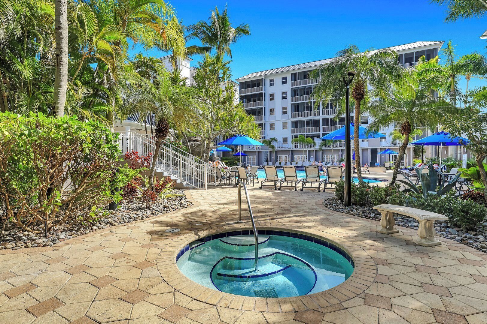 Un espace piscine d’hôtel comprenant un jacuzzi, des chaises longues et des palmiers.