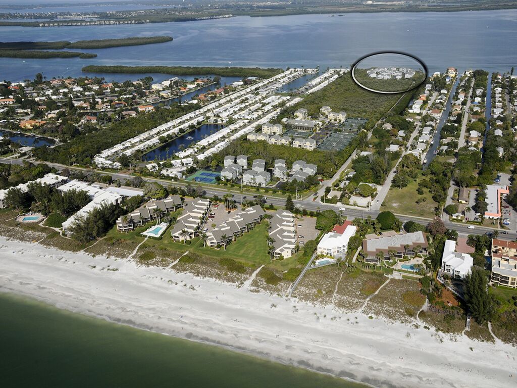 Vue aérienne d’une zone résidentielle côtière, avec un port de plaisance, des maisons et une plage.