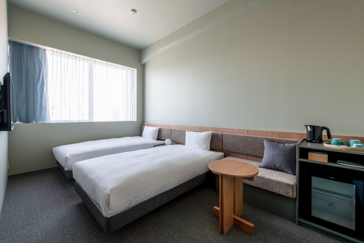 A hotel room with two beds, a sofa, a small round table, and a kitchenette.
