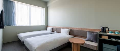 Habitación de hotel con dos camas, un sofá, una pequeña mesa redonda y una kitchenette.