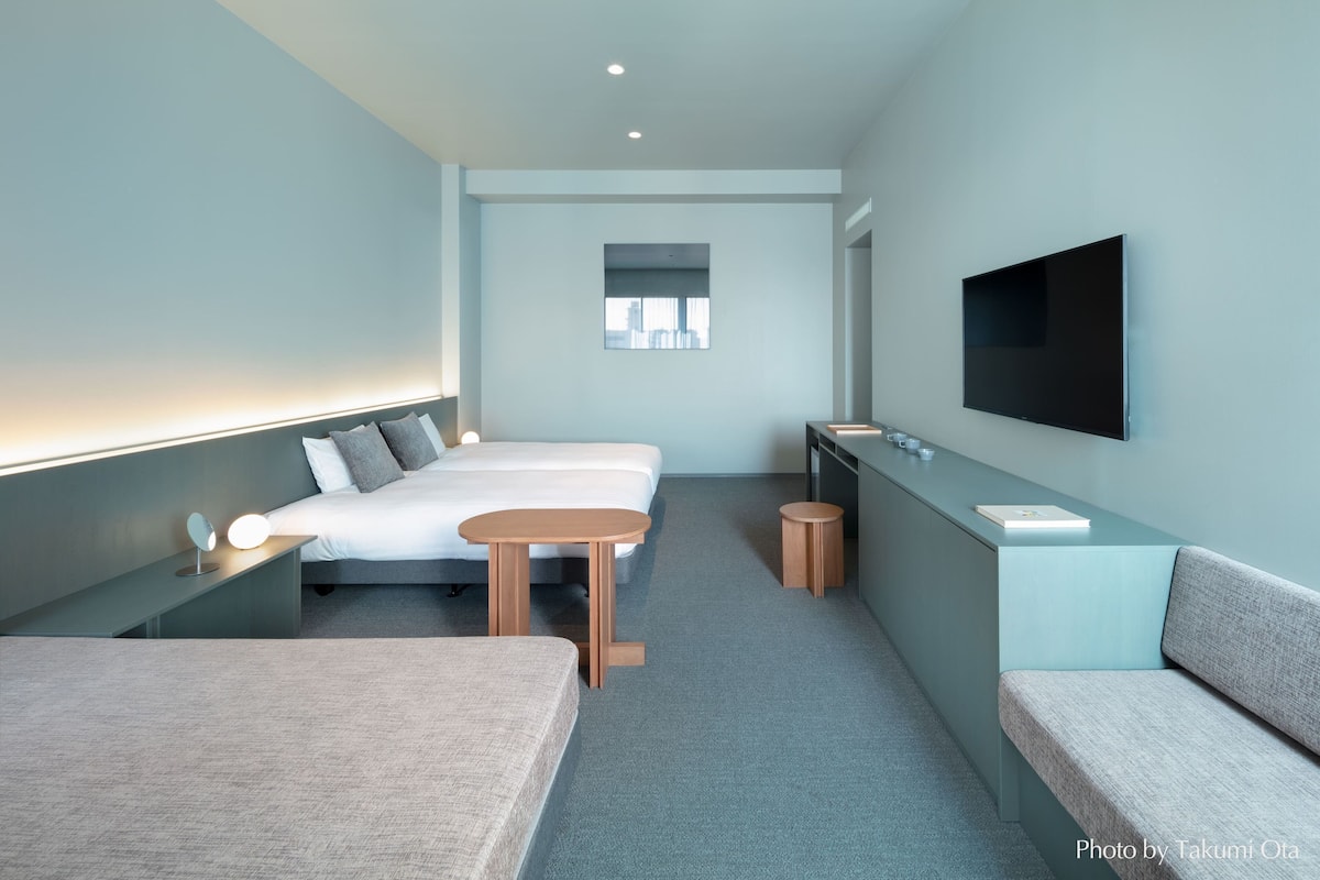 A modern hotel room with a bed, bedside table, and a TV mounted on the wall.