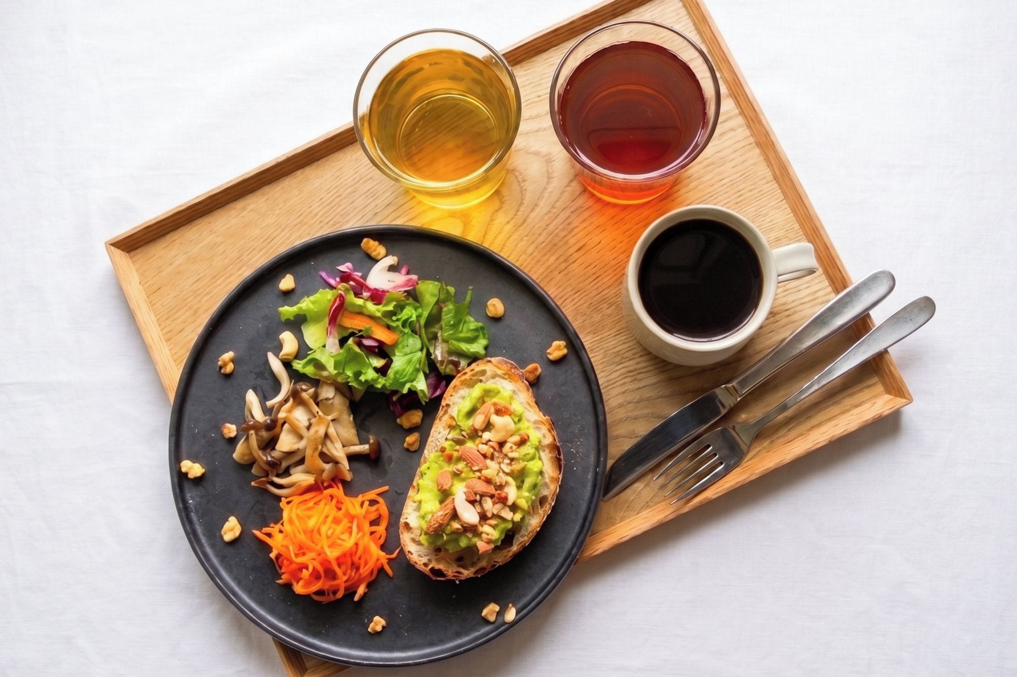 A meal with a salad, bread, and two drinks on a wooden tray.