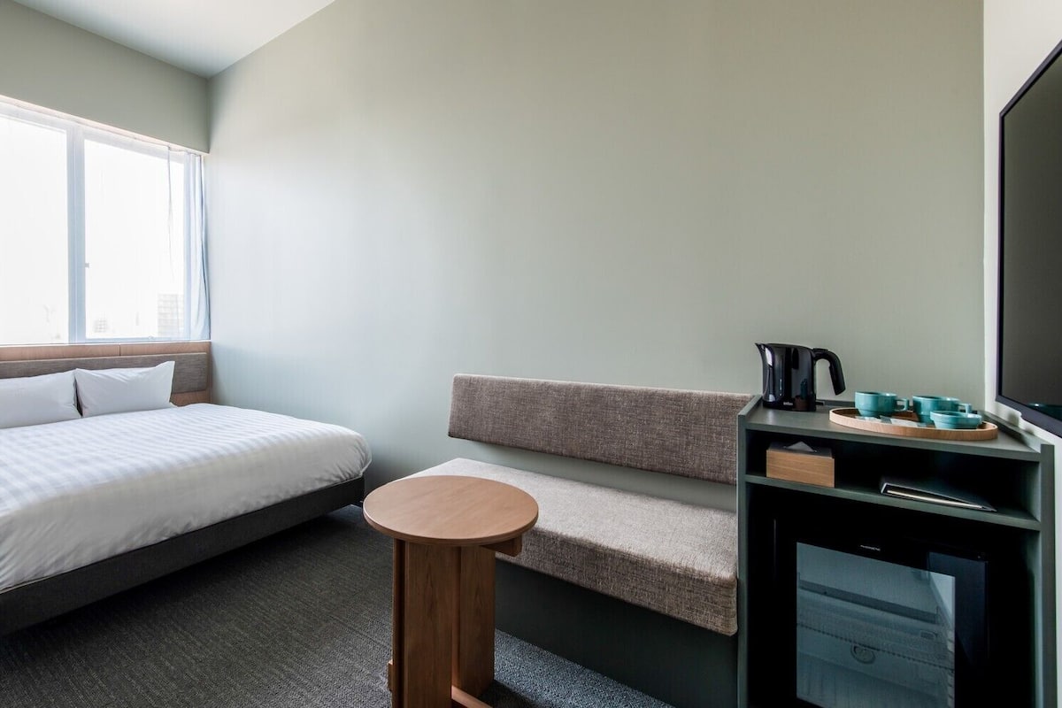 A hotel room with a bed, a seating area, a small table, a TV, and a coffee maker.